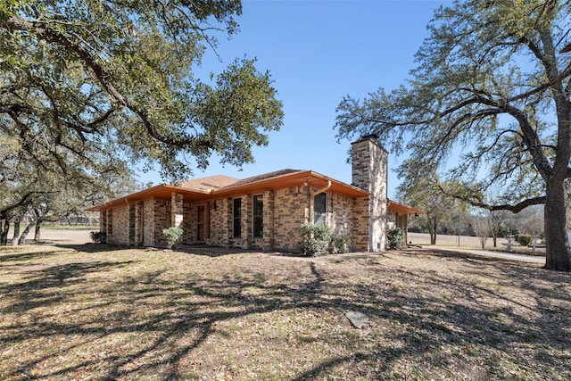 exterior space with brick siding, a lawn, and a chimney