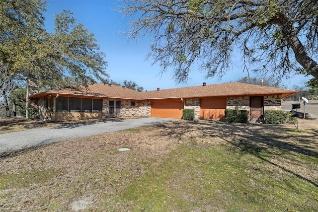 view of front facade featuring stone siding, aphalt driveway, a front lawn, and a sunroom