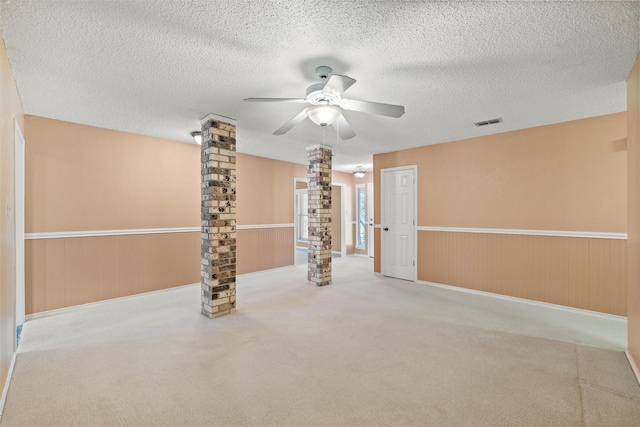 carpeted empty room featuring a wainscoted wall, a textured ceiling, and ornate columns