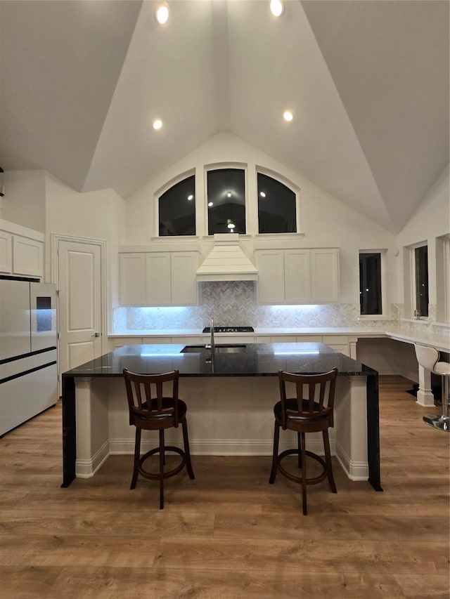 kitchen featuring wood finished floors, a kitchen bar, custom exhaust hood, and white cabinets