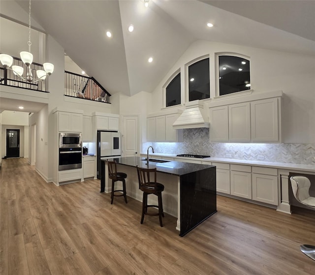 kitchen with custom exhaust hood, stainless steel appliances, white cabinets, a sink, and a kitchen breakfast bar