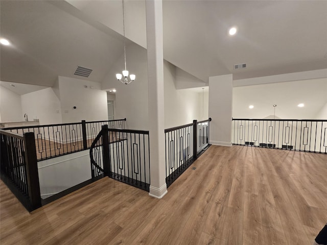 hall featuring a chandelier, visible vents, baseboards, and wood finished floors