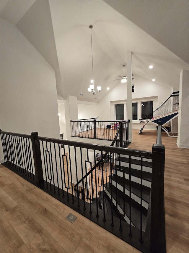 staircase with vaulted ceiling, ceiling fan with notable chandelier, wood finished floors, and recessed lighting