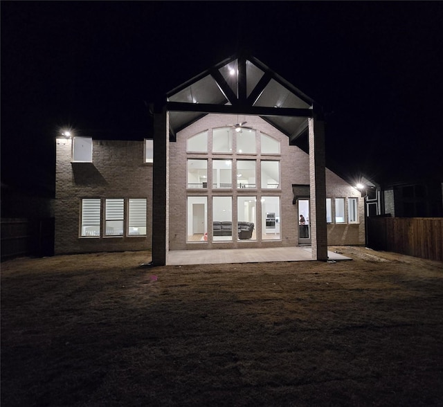 back of house at night featuring a patio, a lawn, and fence