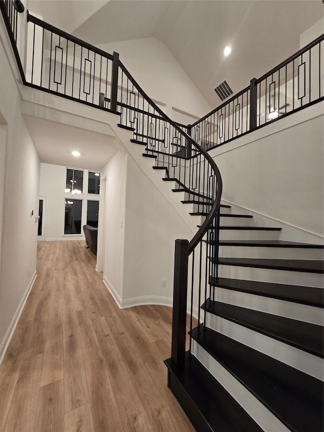 stairs featuring baseboards, visible vents, high vaulted ceiling, and wood finished floors