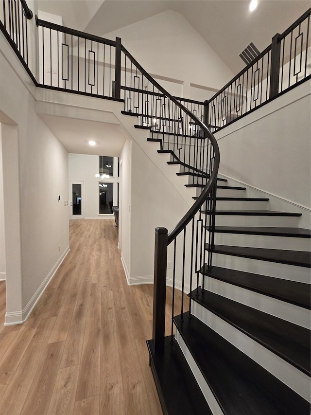 stairs featuring wood finished floors, a towering ceiling, and baseboards