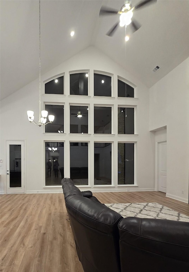 living room featuring baseboards, visible vents, wood finished floors, high vaulted ceiling, and ceiling fan with notable chandelier