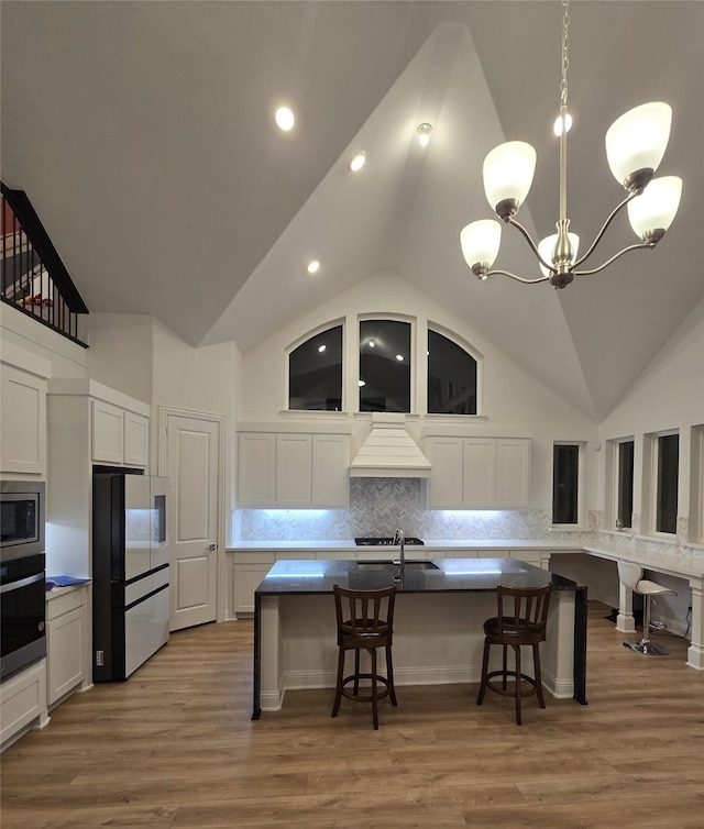 kitchen featuring wall oven, stainless steel microwave, freestanding refrigerator, premium range hood, and a sink