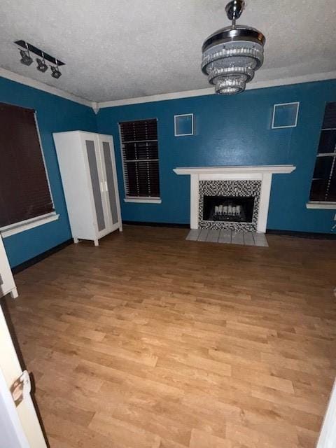 unfurnished living room with a chandelier, a tile fireplace, crown molding, and a textured ceiling