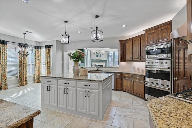 kitchen featuring arched walkways, appliances with stainless steel finishes, wall chimney exhaust hood, a notable chandelier, and recessed lighting