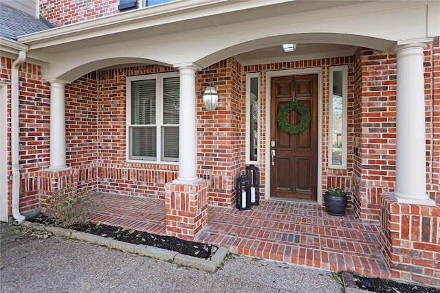 view of exterior entry featuring a porch, brick siding, and a shingled roof