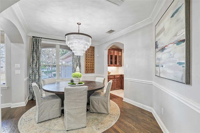 dining area with dark wood finished floors, arched walkways, ornamental molding, and an inviting chandelier