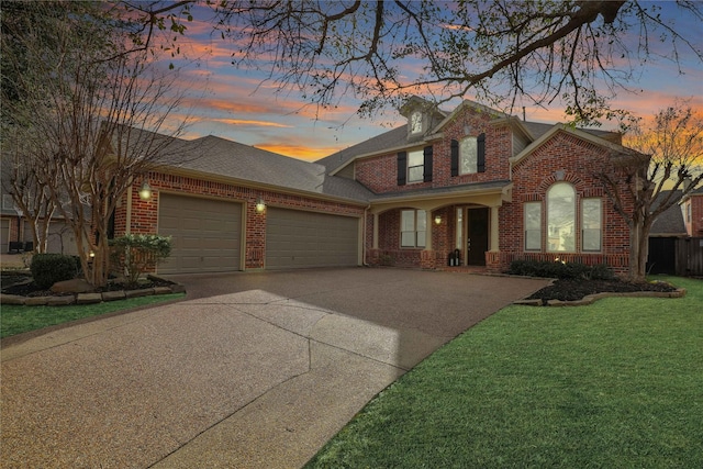 traditional home featuring a shingled roof, a yard, an attached garage, driveway, and brick siding