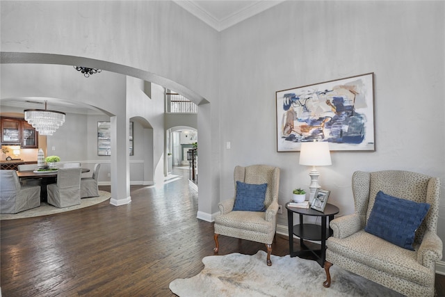 living area featuring arched walkways, a towering ceiling, baseboards, hardwood / wood-style floors, and ornamental molding