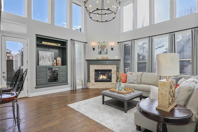 living room with baseboards, a chandelier, wood finished floors, a high ceiling, and a stone fireplace