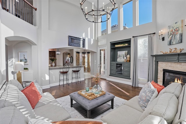 living room with a stone fireplace, wood finished floors, a chandelier, baseboards, and a high ceiling