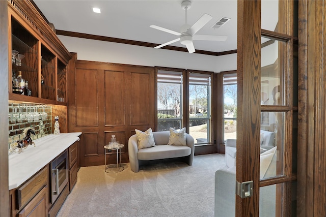 sitting room with light carpet, ceiling fan, ornamental molding, and visible vents