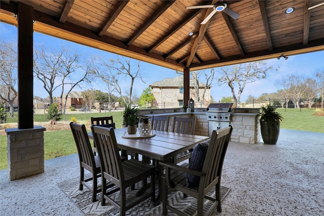 view of patio / terrace featuring an outdoor kitchen, a ceiling fan, a grill, fence, and outdoor dining space