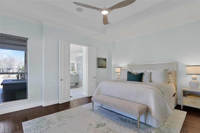 bedroom featuring baseboards, ensuite bath, ceiling fan, wood finished floors, and a tray ceiling