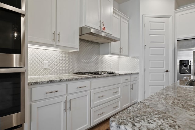 kitchen with decorative backsplash, light stone counters, stainless steel appliances, under cabinet range hood, and white cabinetry