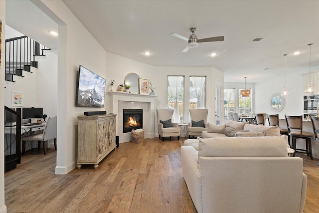 living area with recessed lighting, light wood-style flooring, a ceiling fan, and a glass covered fireplace