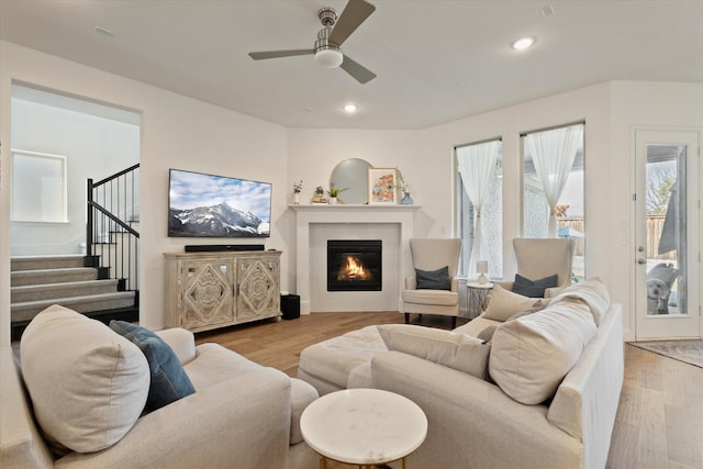 living area with a glass covered fireplace, stairway, wood finished floors, and recessed lighting