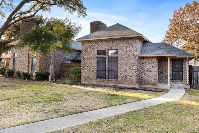 view of front of property with brick siding, a chimney, a shingled roof, a front yard, and fence