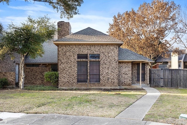 view of front facade with brick siding, fence, roof with shingles, a front lawn, and a chimney