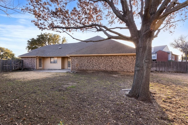 rear view of house featuring a patio, a shingled roof, a fenced backyard, and brick siding