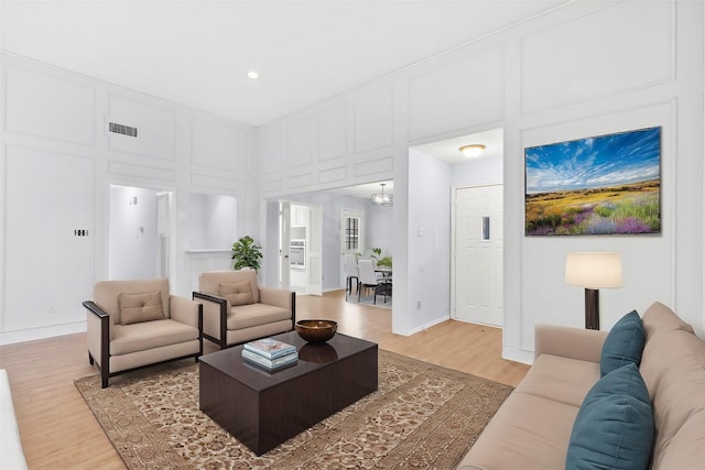 living room featuring visible vents, a decorative wall, light wood-style flooring, and baseboards