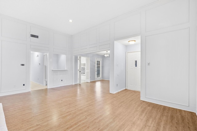 empty room with visible vents, a decorative wall, and light wood finished floors