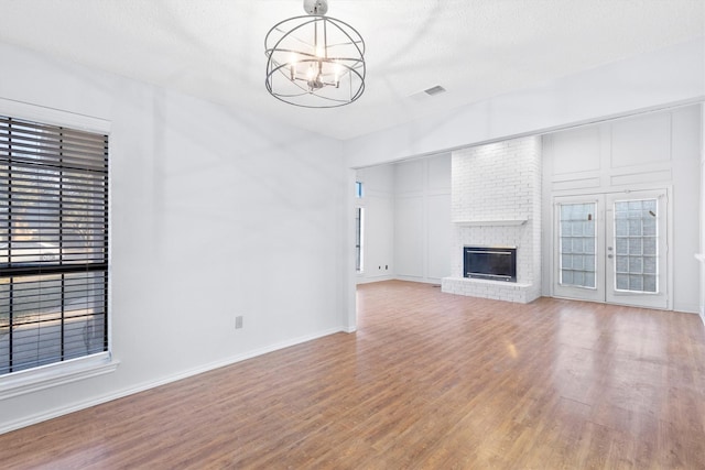 unfurnished living room featuring baseboards, visible vents, wood finished floors, a fireplace, and a chandelier