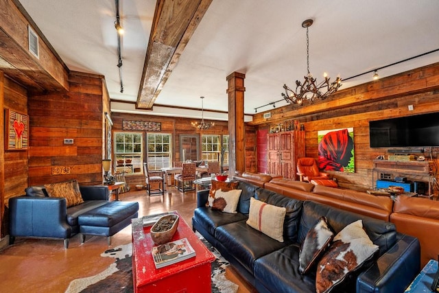 living room featuring ornate columns, rail lighting, finished concrete floors, wood walls, and a chandelier