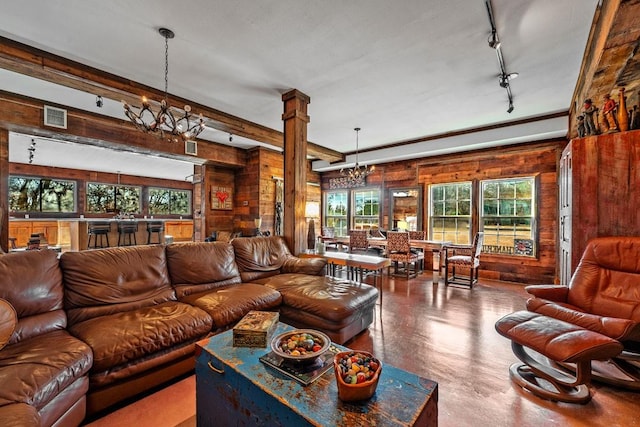 living area with decorative columns, visible vents, an inviting chandelier, wooden walls, and concrete flooring