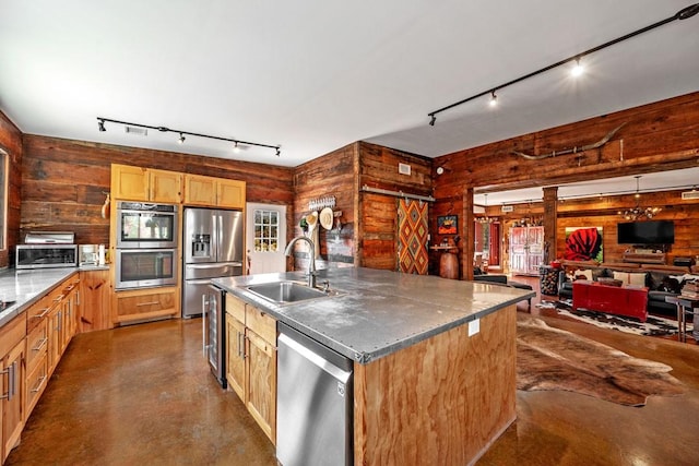 kitchen featuring concrete flooring, stainless steel appliances, wood walls, a sink, and an island with sink