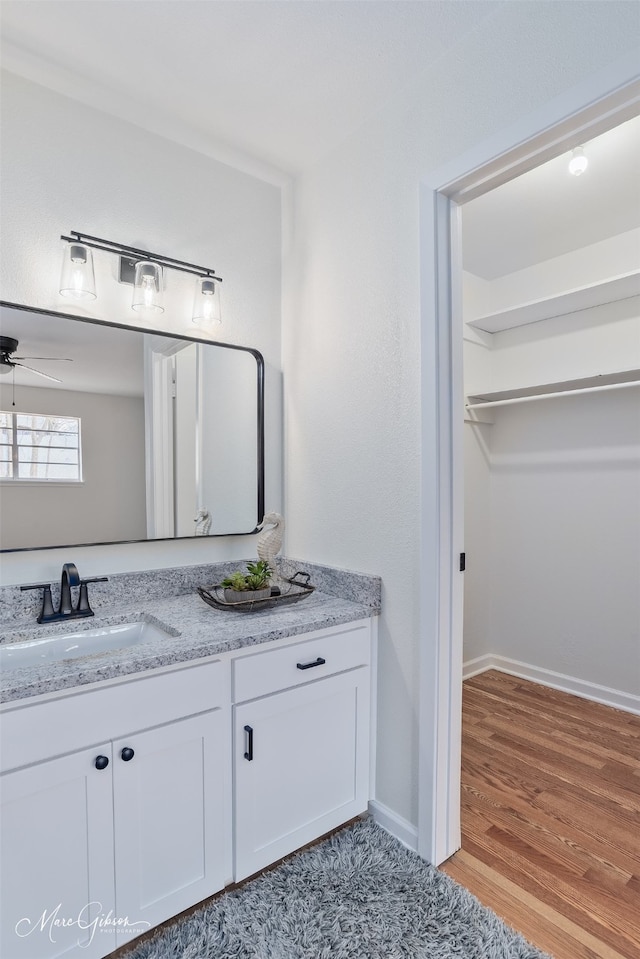 bathroom featuring ceiling fan, vanity, baseboards, and wood finished floors