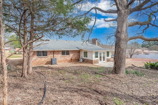 back of property with french doors, a chimney, central AC unit, and brick siding