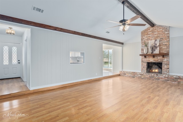 unfurnished living room with a brick fireplace, wood finished floors, visible vents, and a ceiling fan