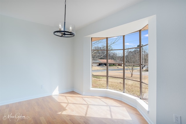 unfurnished dining area with baseboards, a healthy amount of sunlight, an inviting chandelier, and wood finished floors