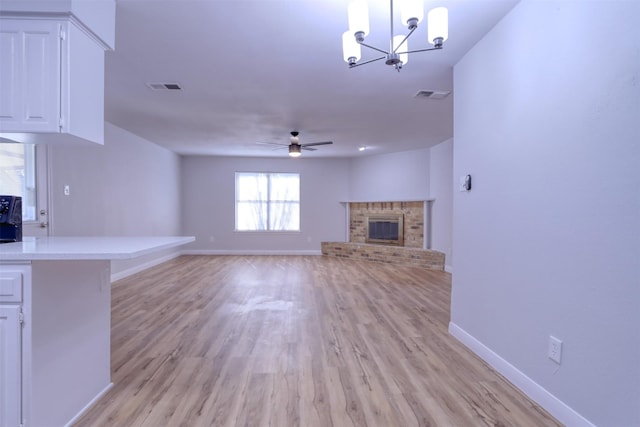 unfurnished living room with baseboards, a fireplace, visible vents, and ceiling fan with notable chandelier