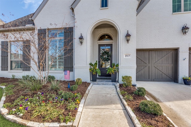 entrance to property with a garage, a shingled roof, concrete driveway, and brick siding