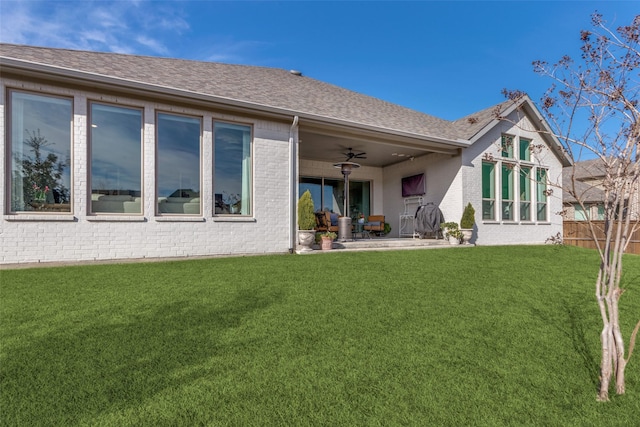 rear view of property featuring brick siding, a ceiling fan, roof with shingles, a lawn, and a patio area