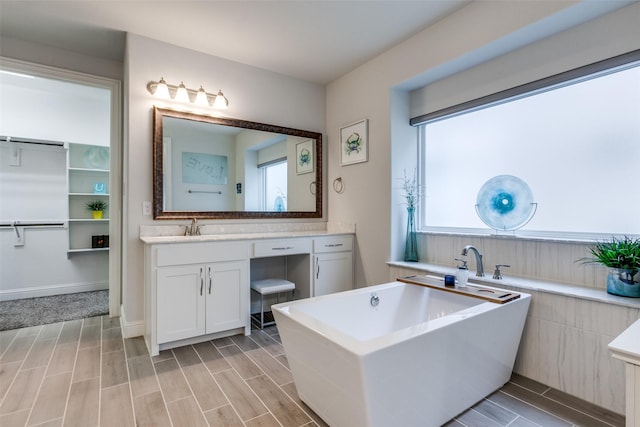 bathroom featuring wood tiled floor, a freestanding tub, vanity, and baseboards