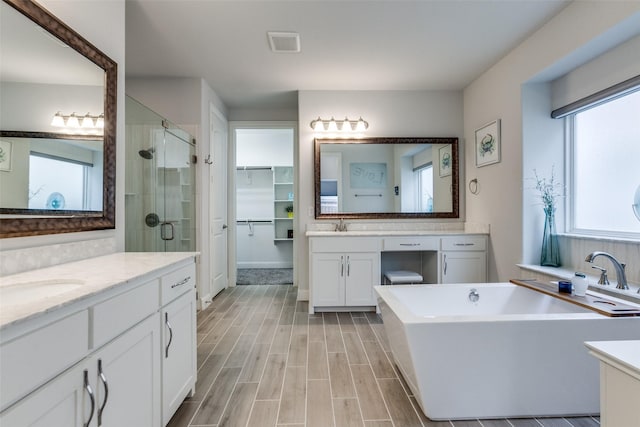 full bath featuring visible vents, a freestanding bath, wood tiled floor, a sink, and a shower stall