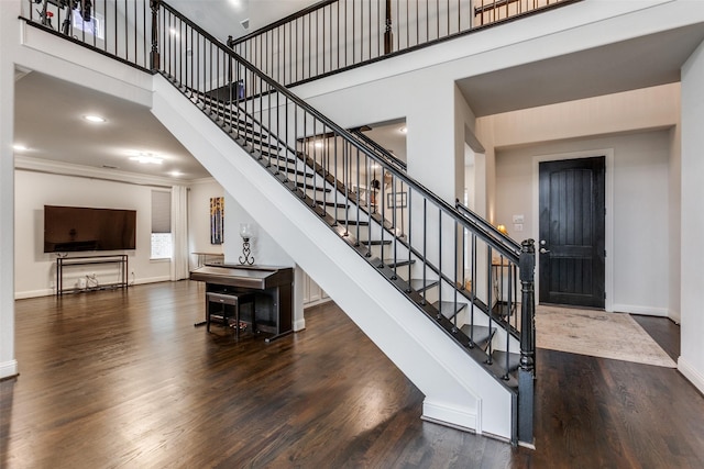 stairway with ornamental molding, a high ceiling, baseboards, and wood finished floors