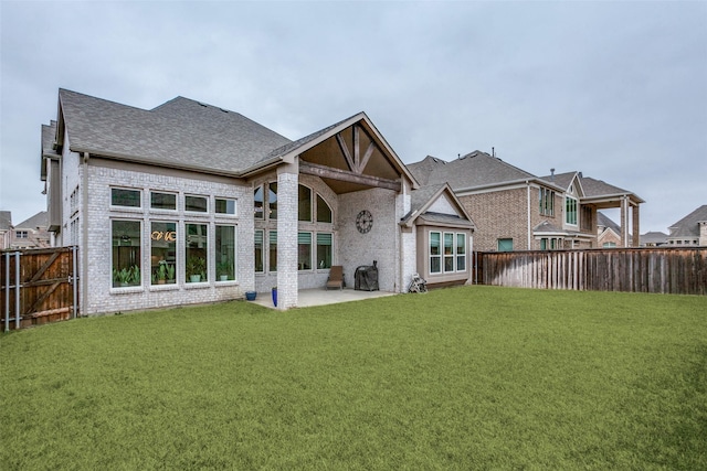 back of property with a yard, a fenced backyard, roof with shingles, and brick siding