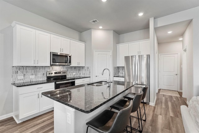 kitchen with appliances with stainless steel finishes, a breakfast bar, wood finished floors, a sink, and backsplash