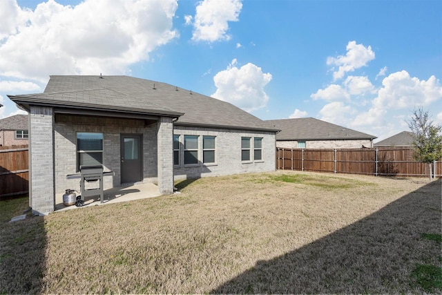 rear view of property with brick siding, a yard, a fenced backyard, and a patio