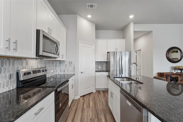 kitchen featuring dark stone countertops, stainless steel appliances, a sink, and wood finished floors