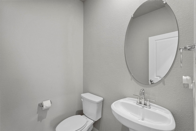 half bath with a textured wall, a sink, and toilet